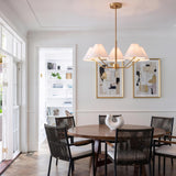 A transitional dining room with the Wallace 5 Light Chandelier in satin brass with white linen shades over a round wood table and woven chairs.