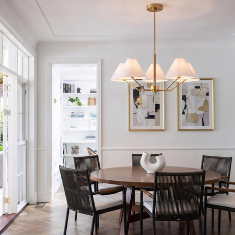 A transitional dining room with the Wallace 5 Light Chandelier in satin brass with white linen shades over a round wood table and woven chairs.