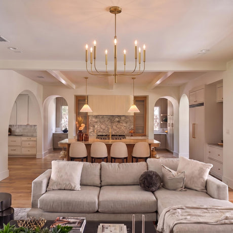 A Mediterranean living room with a brushed brass chandelier along the ceiling above a neutral sectional sofa, featuring arched doorways leading to a beamed kitchen with marble.