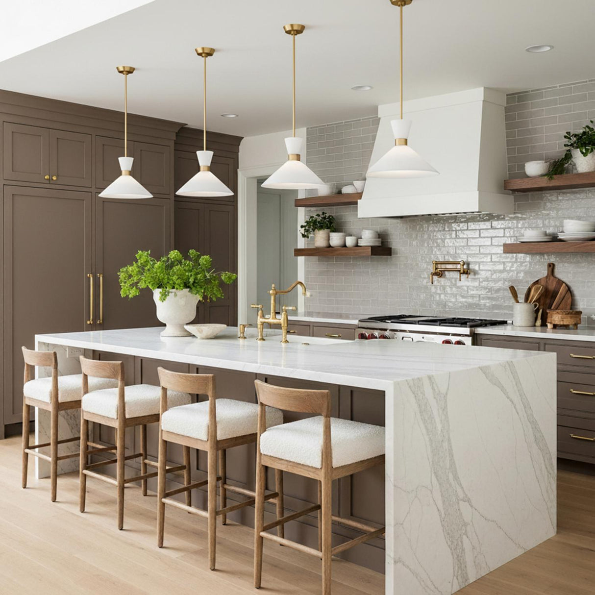A transitional kitchen featuring four Issa Pendant 15" Satin Brass cone pendants with white glass shades suspended over a white marble waterfall island and gray tile backsplash.
