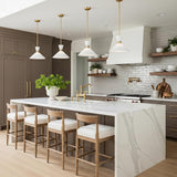 A transitional kitchen featuring four Issa Pendant 15" Satin Brass cone pendants with white glass shades suspended over a white marble waterfall island and gray tile backsplash.