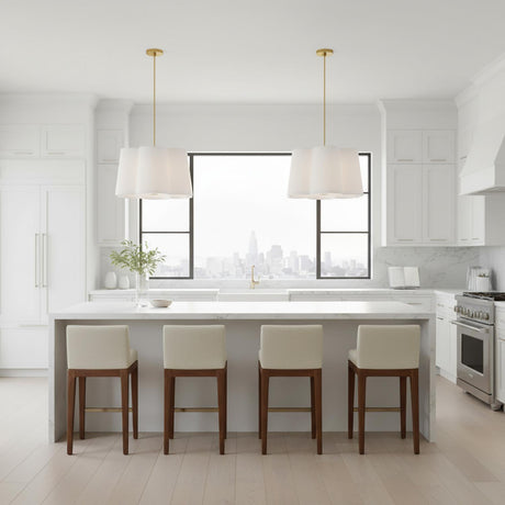 Odelia Large Pendant 28, White and Brass - Two white lamps with brass accents hang over a white kitchen island with four cream-colored bar stools and a cityscape visible through a large window.