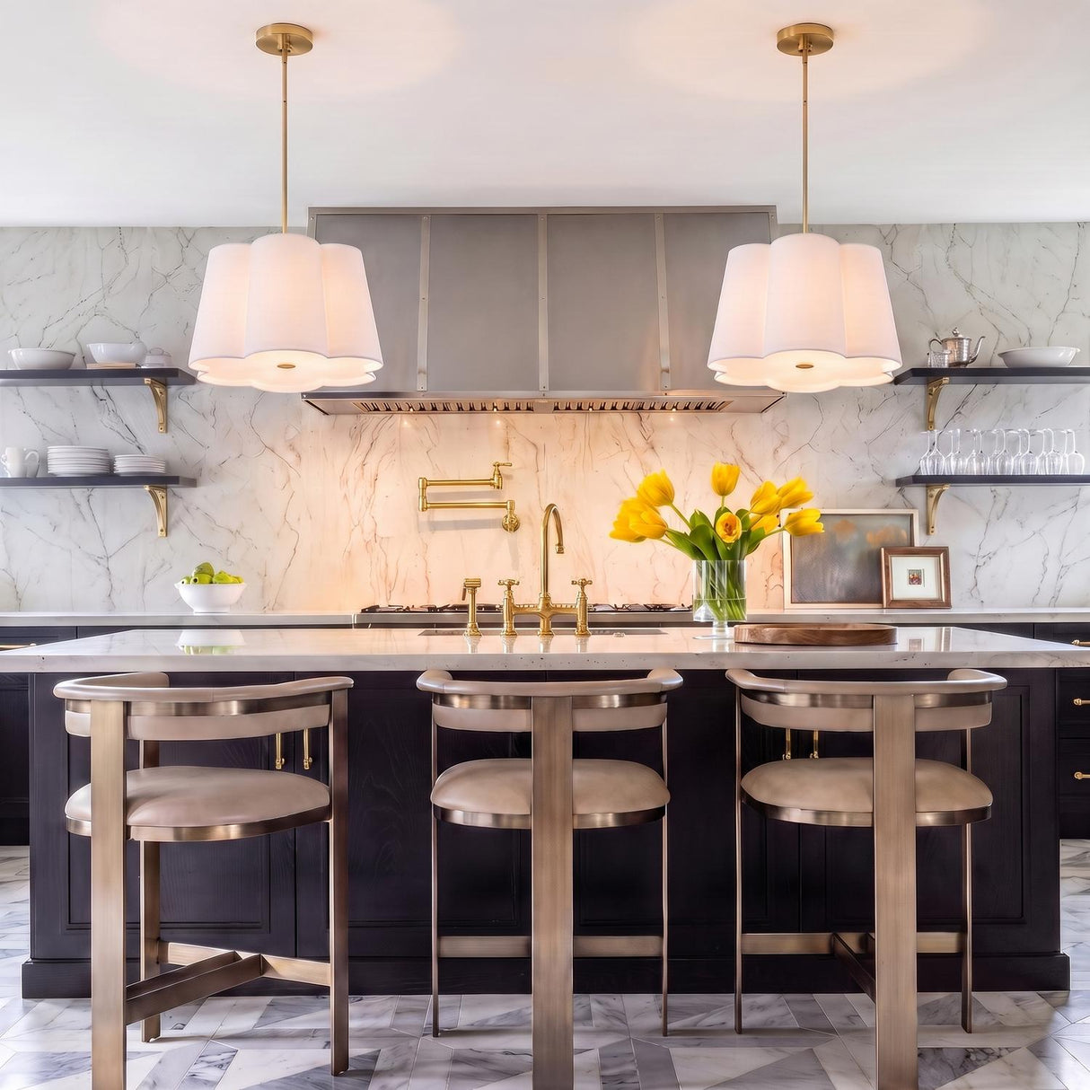 A transitional kitchen with two white Odelia Medium Pendant 22", White and Brass fixtures over a white marble island with black cabinets and a gold pot filler.