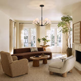A contemporary living room featuring the Wallace 5 Light Chandelier 30 inch in matte black with white linen shades centered above a curved brown sofa near French doors.