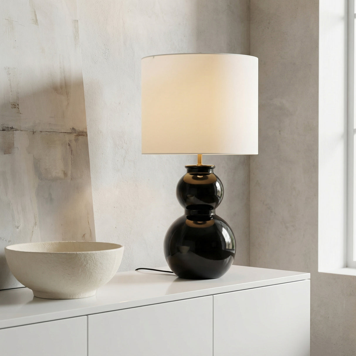 Truett Table Lamp 27", Glossy Black geometric Table Lamp in a Modern Living Room with a white minimalist credenza & textured neutral bowl.
