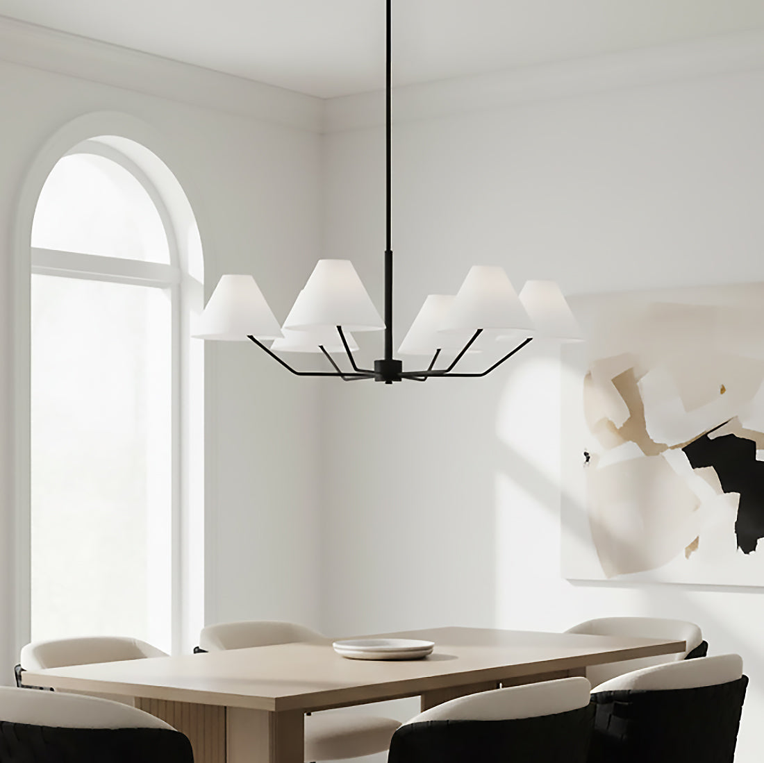 Wallace 6 Light Chandelier 38, Matte Black - A matte black chandelier with white conical shades hangs above a light wood dining table with upholstered chairs, with a large arched window in the background and abstract art on the wall.
