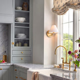 A traditional kitchen featuring the Wallace Wall Sconce 8", Satin Brass with a white linen shade mounted beside a window over a marble farmhouse sink.