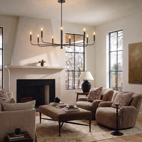 A modern farmhouse living room with an antique iron Thayer 9 Light Chandelier 48" centered over a tan ottoman coffee table beside a white plaster fireplace.