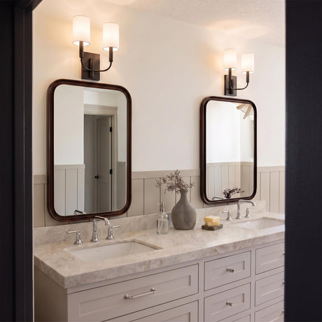 A transitional bathroom with two Thayer Double Wall Sconces in an antique iron finish and linen shades above rounded mirrors, a marble vanity, and wainscoting.