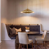 A transitional dining area with a brushed brass saucer pendant over a dark round table surrounded by a plaid banquette and vertical paneled walls.