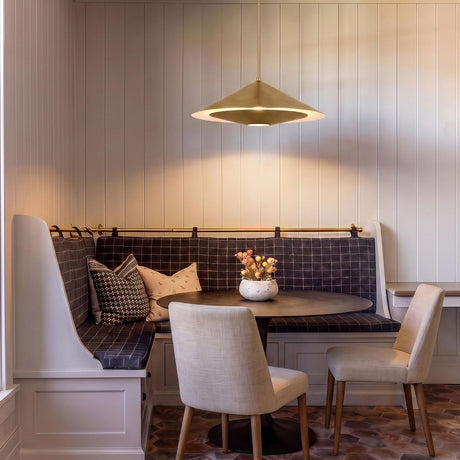 A transitional dining area with a brushed brass saucer pendant over a dark round table surrounded by a plaid banquette and vertical paneled walls.