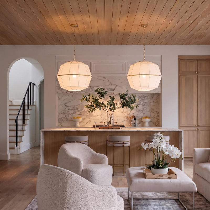 A transitional kitchen with two Birch Large Pendants in modern brass and white linen over a marble waterfall island under a light wood-slat ceiling.
