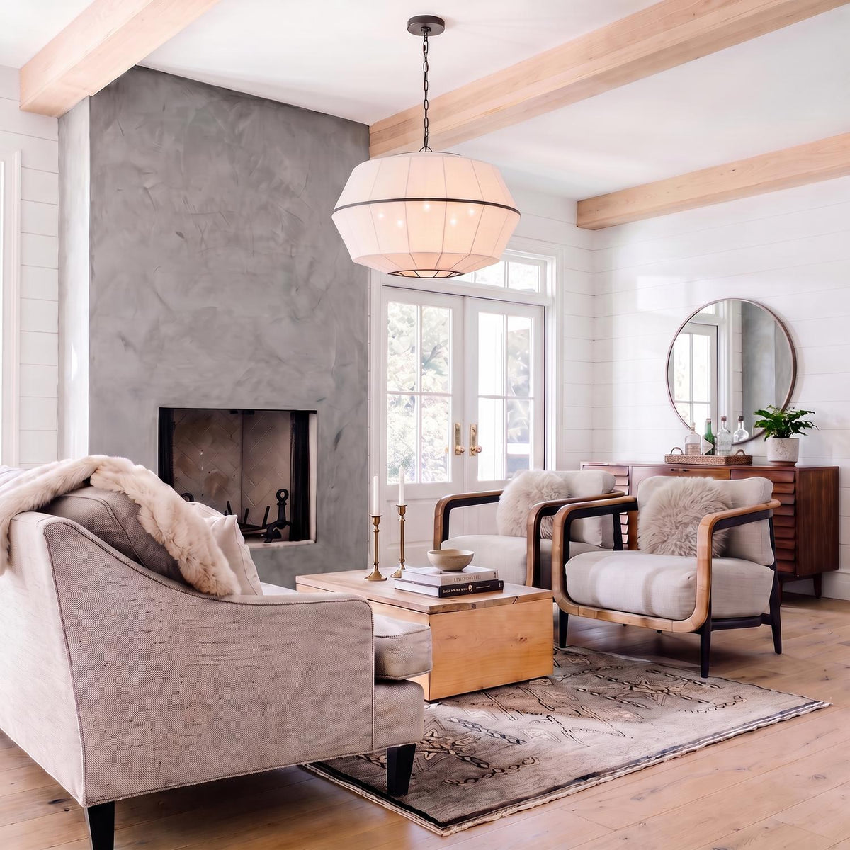 A modern farmhouse living room features a white linen pendant with aged iron trim suspended from wood ceiling beams near a large concrete fireplace.