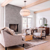 A modern farmhouse living room features a white linen pendant with aged iron trim suspended from wood ceiling beams near a large concrete fireplace.
