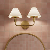 Dean 2 Light Vanity - A brass and opal glass vanity light above a round gold mirror against a pink tiled wall.