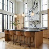 A modern kitchen featuring three Merrick Pendant 8", Modern Brass globe pendants with brushed brass hardware over a wood island with dark counters under a double-height ceiling.