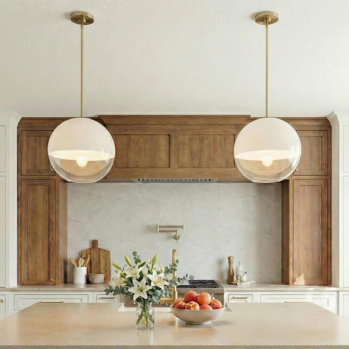 A contemporary kitchen featuring two Merrick Pendant 14", Modern Brass globe pendants with glass shades suspended over a beige island in front of wood cabinetry and backsplash.