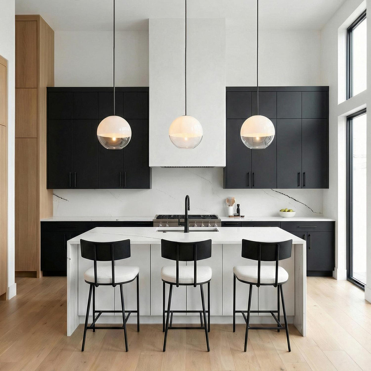 A modern kitchen featuring three frosted glass Merrick Pendant 14 inch Aged Iron fixtures over a white marble waterfall island with matte black cabinets.