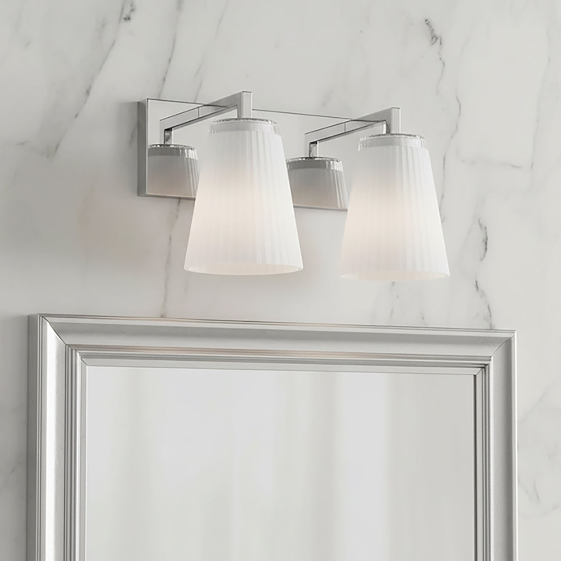 Margot 2 Light Vanity, Chrome - Two ribbed white conical shades with chrome accents mounted on a chrome bar against a marble-patterned wall, reflected in a silver-framed mirror.