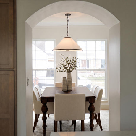 A transitional dining room features a white linen pendant with aged iron trim over a dark wood table and cream chairs viewed through an arched entryway.
