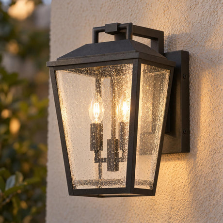 A transitional home exterior featuring the Harrison Outdoor Medium Wall Light 14", Textured Black glowing against a beige stucco wall near garden foliage at dusk.