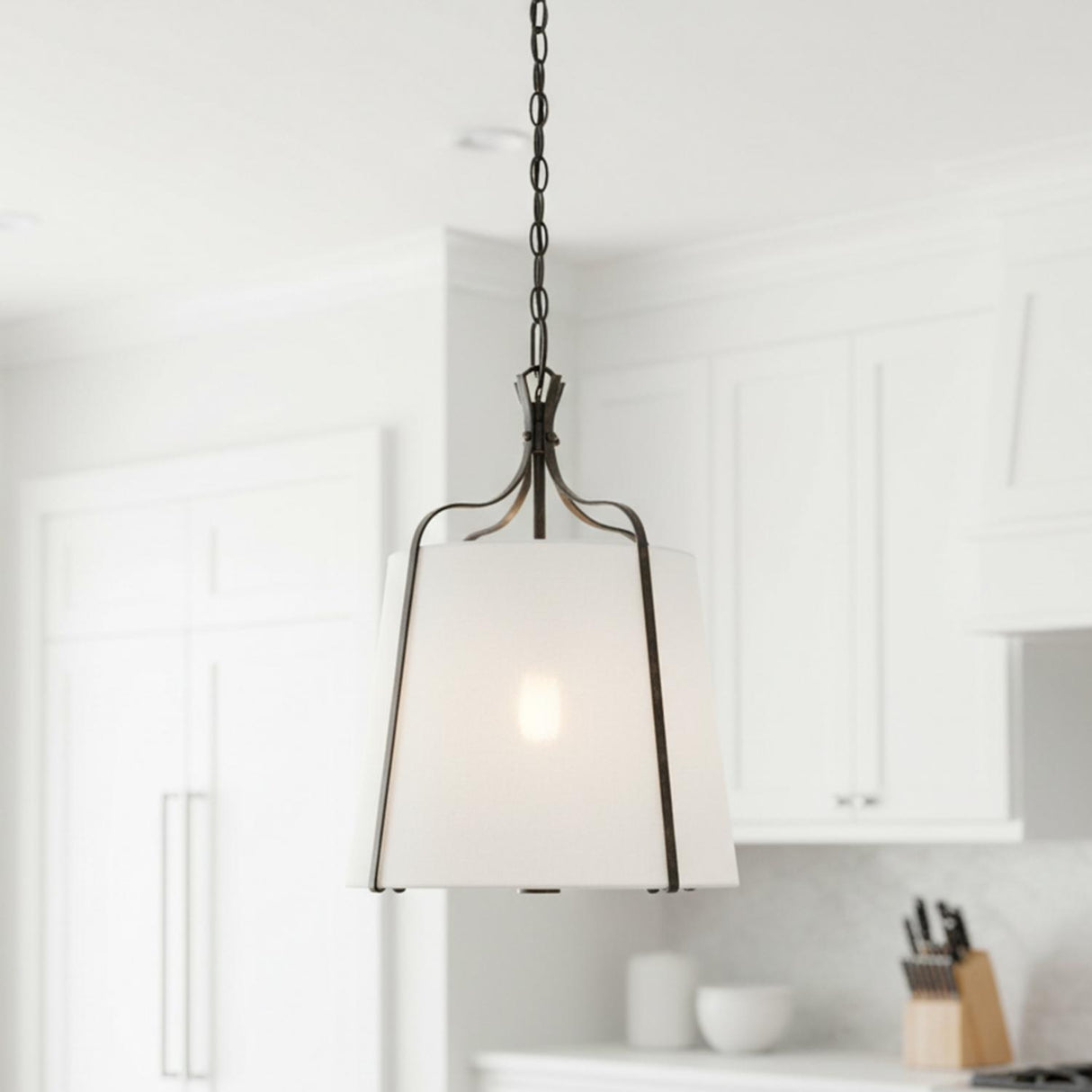 A transitional kitchen featuring the Isleton Small Pendant 14 inch in Aged Steel with a white linen shade over the island and white cabinetry.