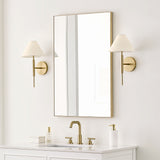 Two 17" tall Hazelton Wall Sconces in Satin Brass with white fabric shades flanking a rectangular gold framed vanity mirror in a bright bathroom
