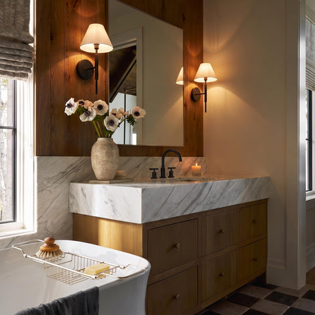 A modern farmhouse bathroom with two Hazelton Wall Sconces in matte black with linen shades flanking a mirror above a marble vanity and wood-planked wall.
