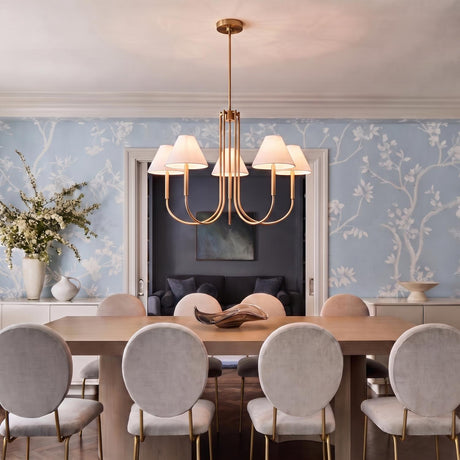 A traditional dining room with the Hazelton 5 Light Chandelier in satin brass with linen shades hanging over a wood table against blue floral wallpaper.