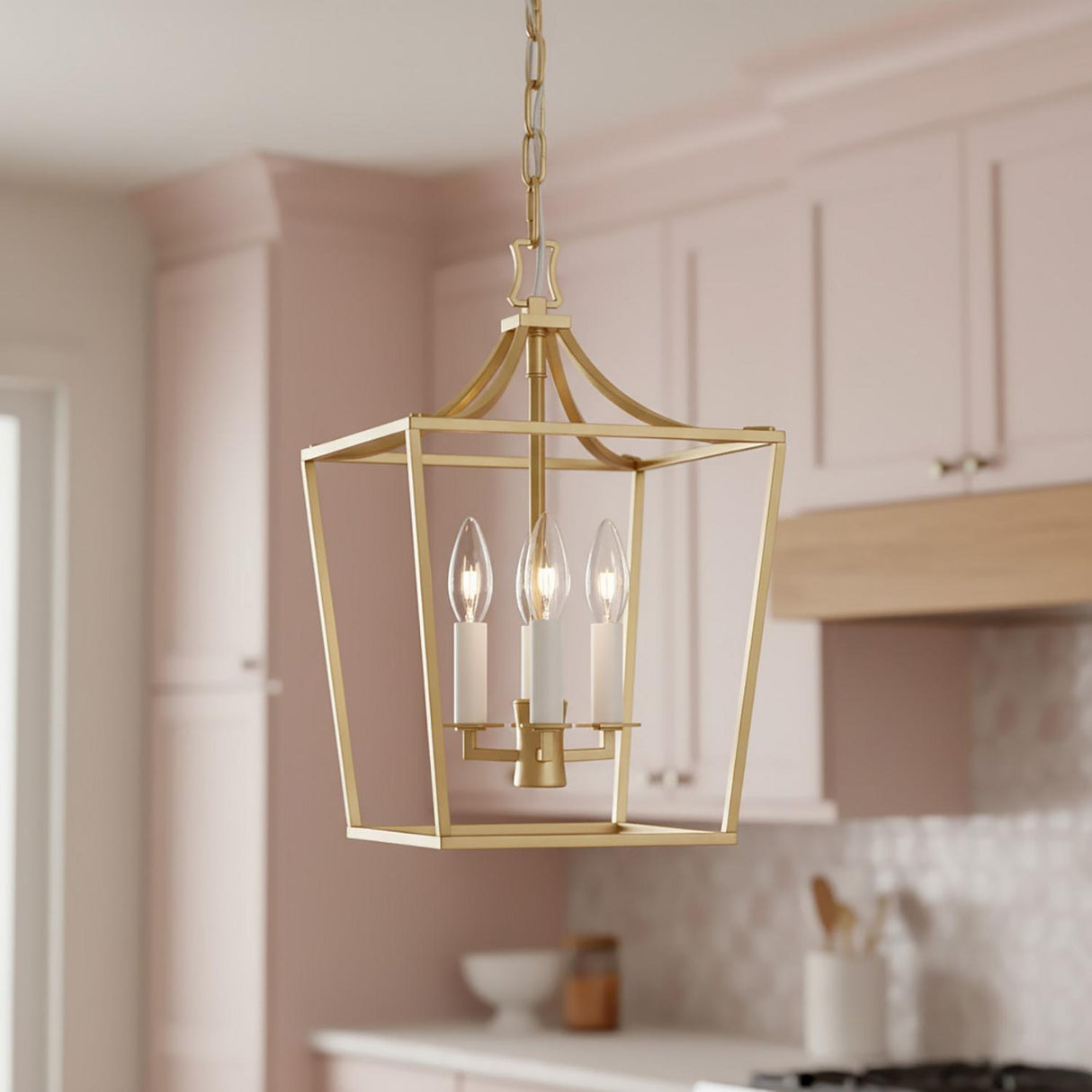 A transitional kitchen features the Grayden Small Lantern Pendant 10", Modern Brass suspended along the ceiling near blush pink cabinets and a white mosaic tile backsplash.