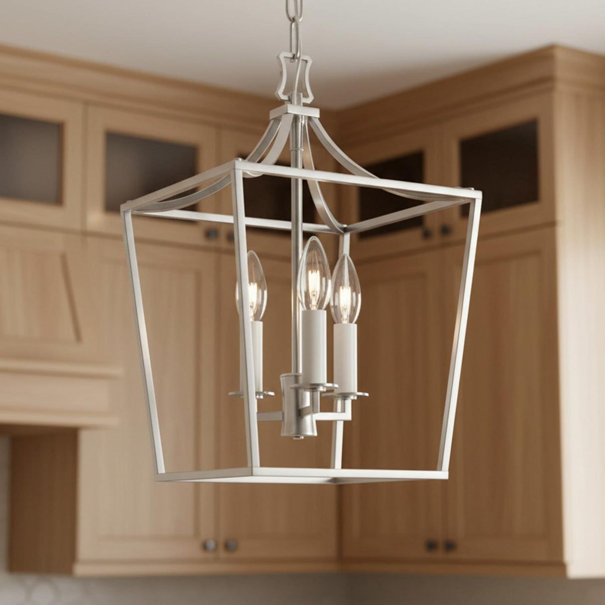 A transitional kitchen features the Grayden Small Lantern Pendant 10 inch Polished Nickel hanging along the ceiling in front of light wood shaker cabinets with glass inserts.