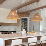 A coastal kitchen with two Paloma Pendant 22" Modern Brass and Rattan pendants over a white marble waterfall island with white cabinetry and a beamed ceiling.