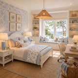 A coastal bedroom features a Paloma Pendant 30", Modern Brass and Rattan over a white bed with blue floral wallpaper and a sunlit window seat.