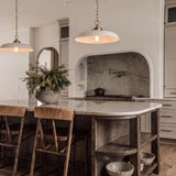 A transitional kitchen with two Franklin Pendant Matte White and Modern Brass fixtures over a white marble island with an arched stone range alcove and wood barstools.