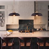 A transitional kitchen with two Franklin Pendant 20", Matte Black and Modern Brass fixtures hanging over a marble island with dark wood woven stools.