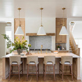A modern farmhouse kitchen with three Classon Medium Pendants in matte white and modern brass over a white marble island with light wood cabinets and shiplap ceiling.
