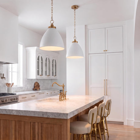 A transitional kitchen features two Rodney Medium Pendant 16", Matte White and Modern Brass lights suspended over a white marble island with reeded wood paneling.