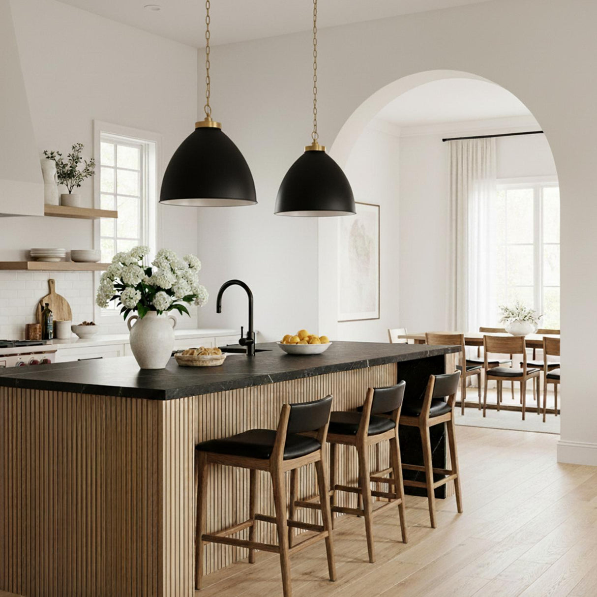 A contemporary kitchen with two Rodney Large Pendant 18", Matte Black and Modern Brass over a slatted wood island featuring a black marble counter and arched entryway.