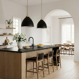 A contemporary kitchen with two Rodney Large Pendant 18", Matte Black and Modern Brass over a slatted wood island featuring a black marble counter and arched entryway.