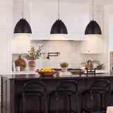 A transitional kitchen features three Rodney Large Pendants in Matte Black and Polished Nickel hanging over a dark island with black counter stools.