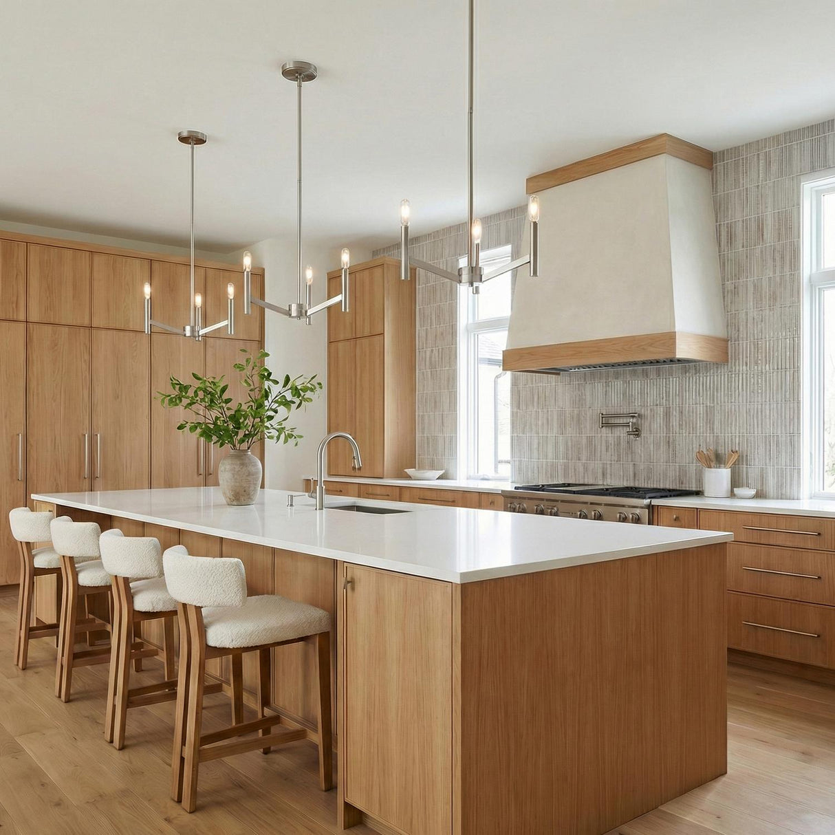 A contemporary kitchen featuring two Foster 3 Light Pendant 18 inch Brushed Nickel fixtures over a white quartz island with natural wood cabinetry and textured tile backsplash.