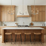 A transitional kitchen features three brushed nickel Foster 3 Light Pendant 18 inch fixtures over a white island with natural wood cabinets and a square tile backsplash.