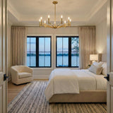 Foster 9 Light Chandelier 36", Satin Brass geometric chandelier in a Transitional Bedroom with a beige upholstered bed and lake view.