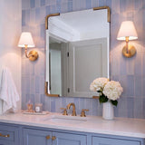 A transitional bathroom vanity features two Harlow Wall Sconce 9", Modern Brass with Rattan lights flanking a brass mirror over blue vertical subway tile.