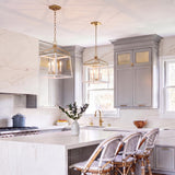 A transitional kitchen with two Fillmore Large Lantern Pendants in matte white and modern brass over a white marble waterfall island and gray shaker cabinets.