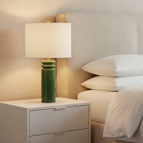 Green Agnes Table Lamp, 26" tall with white shade, on a nightstand next to a bed with white pillows.