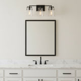 Glyn 3 Light 24" wide Vanity Light, Matte Black and clear glass, shown above a single sink and mirror in a neutral designed bathroom.