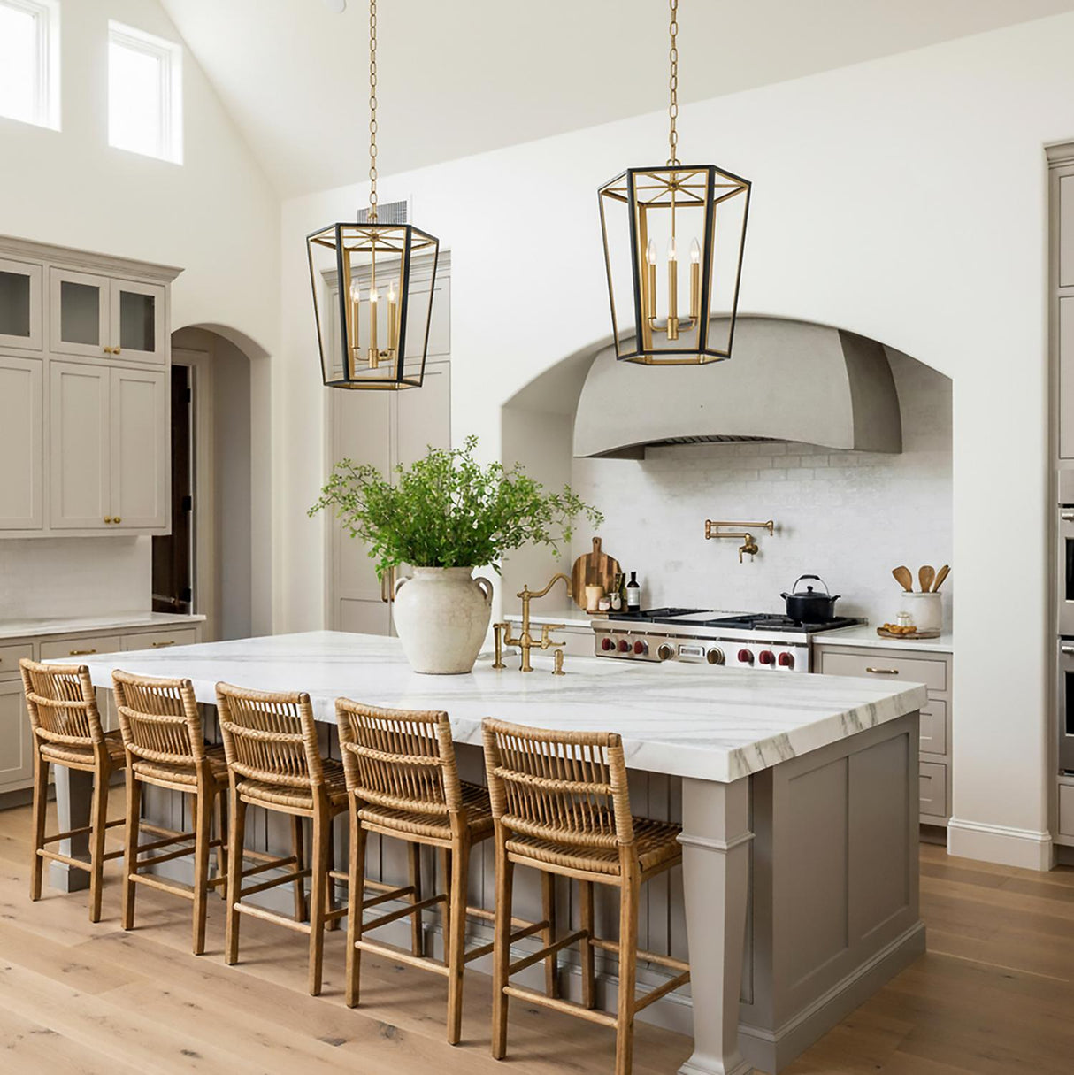 A transitional kitchen featuring two Rawlin Small Lantern Pendants in matte black and brushed brass hanging over a white marble island with woven rattan barstools.