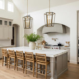 A transitional kitchen featuring two Rawlin Small Lantern Pendants in matte black and brushed brass hanging over a white marble island with woven rattan barstools.