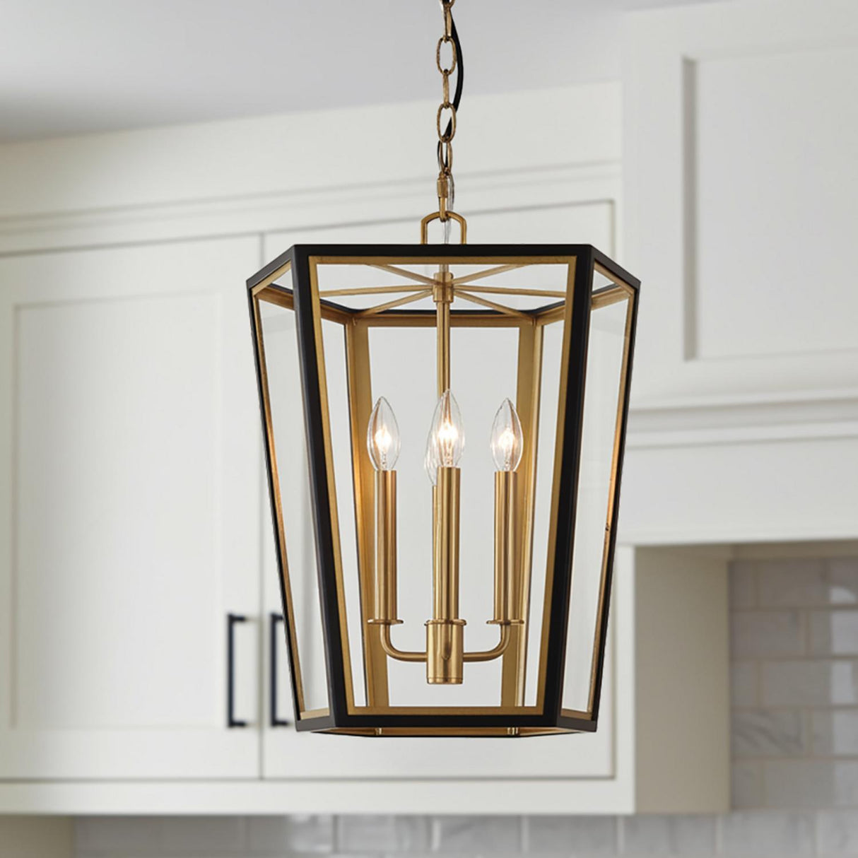 A kitchen featuring a Rawlin Small Lantern Pendant 16", Matte Black and Brushed Brass hanging over the island against white shaker cabinets and a marble tile backsplash.